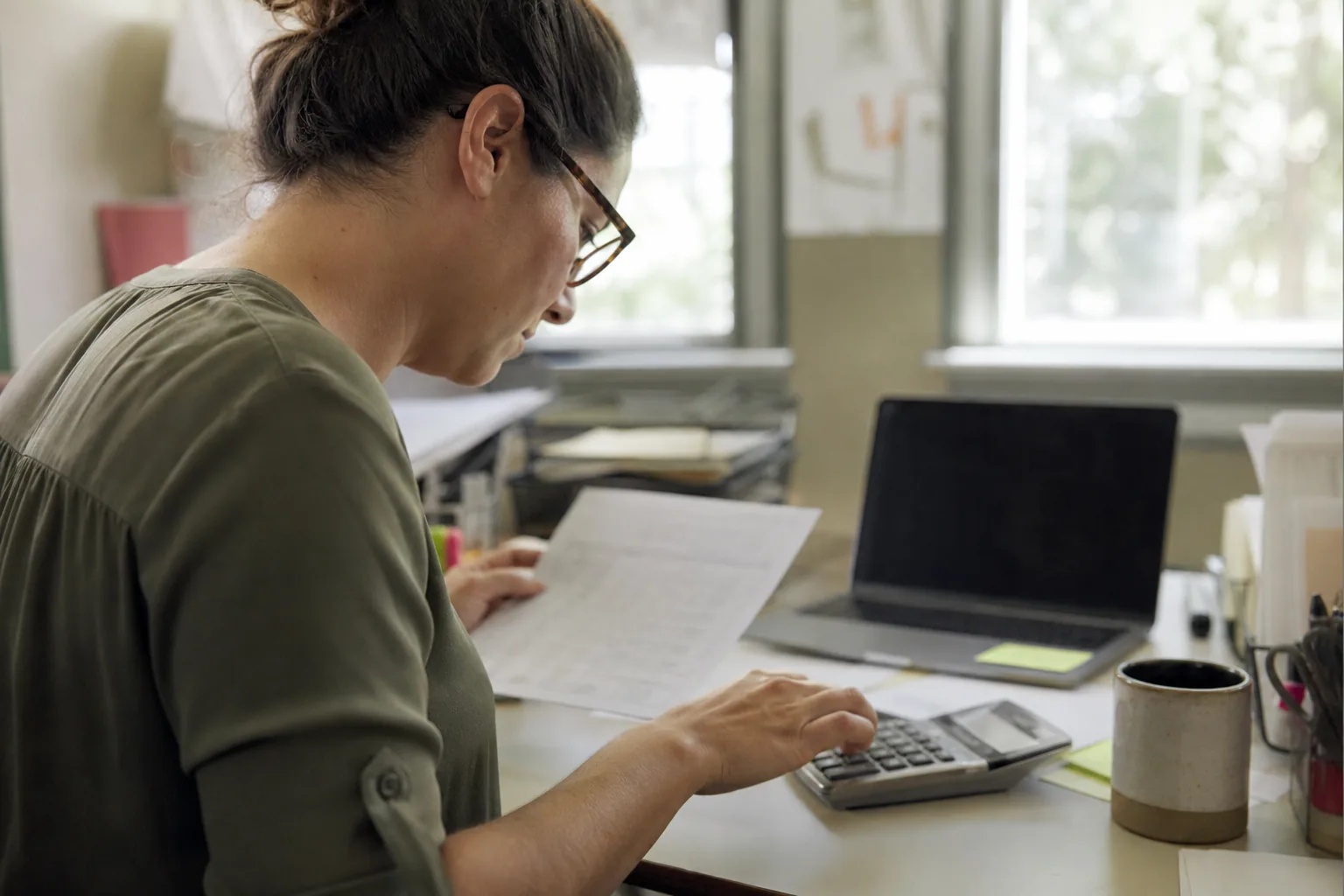 Office manager adding up monthly software seat costs with a calculator and a laptop