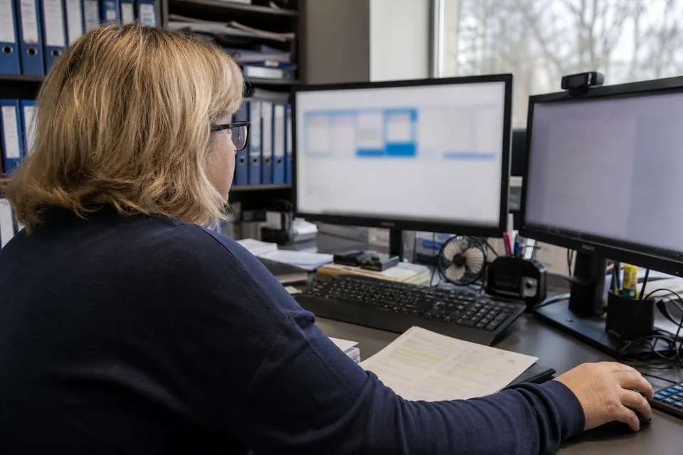 Office manager placing fields on a contract page across two monitors, a highlighted printout beside the keyboard