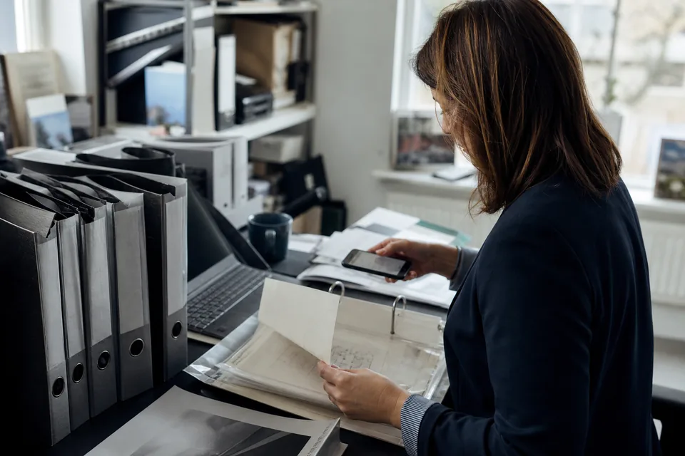 Office manager photographing pages from a ring binder of old contract templates
