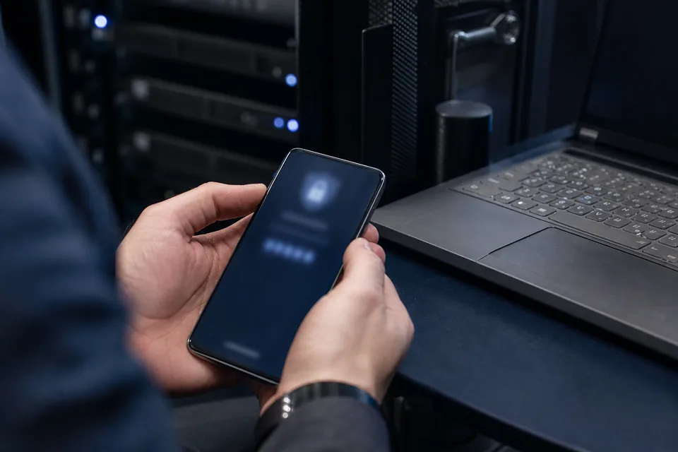 Hands holding a phone with a sign in prompt next to a laptop by a server rack